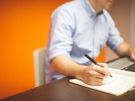 Man writing something down while working on his laptop