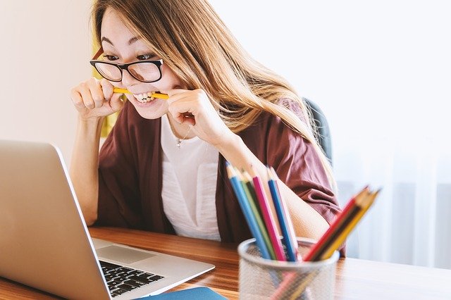 Woman working on a laptop with a pencil in her mouth