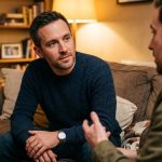 One man thoughtfully listening to another man in a warm environment.